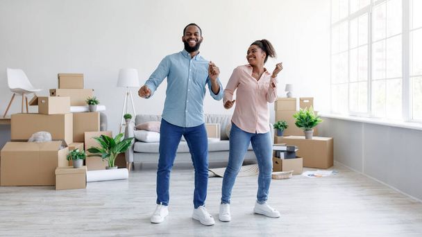 Feliz joven negro macho y dama bailando en nuevo apartamento, celebrando la compra o mudanza a su propia casa - Foto, imagen