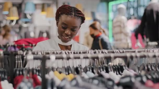 Afro american woman african girl black buyer consumer shopper without medical mask in public place store shop choosing clothes runs across rack of goods dresses buying in shopping mall. Sale discounts - Footage, Video