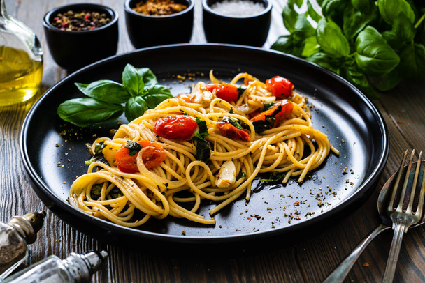 Spaghetti aglio e olio with parmesan, cherry tomatoes and basil on wooden table  - Fotoğraf, Görsel
