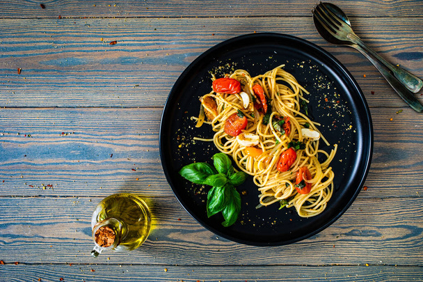 Espaguetis aglio e olio con parmesano, tomates cherry y albahaca sobre mesa de madera  - Foto, imagen