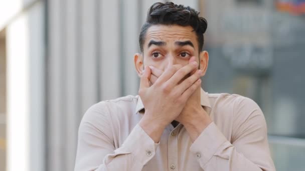 Close-up verwarde mannelijke gezicht latino latino bebaarde man millennial zakenman student baas misdaad getuige sluiten covers mond met handen weigeren om verschrikkelijke geheime beloftes te vertellen geheimhouden stilte - Video