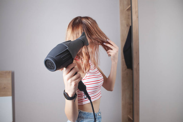 Mädchen trocknet zu Hause Haare mit Haartrockner. - Foto, Bild