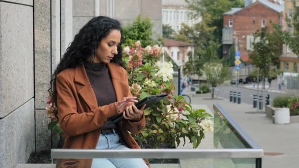 Serious focused busy pensive business woman with digital tablet girl with modern wireless gadget device chat browsing network distant works checking mail sitting on terrace balcony in office outside - Footage, Video