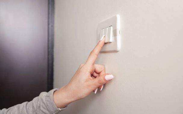 Female hand turning an electricity light switch on the wall. - Foto, imagen