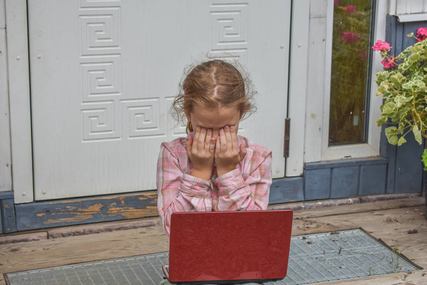a girl child with a laptop is sitting on the porch of the house during a lesson on a remote photo without a filter - Foto, immagini