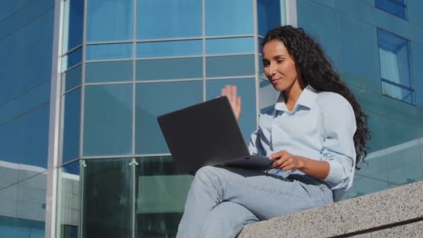 Una joven estudiante usando una laptop sentada afuera en la ciudad. Hermosa mujer de negocios con la computadora que tiene chat de vídeo en línea conversación remota hablando saludar sentarse en la calle ait beso gesto - Metraje, vídeo