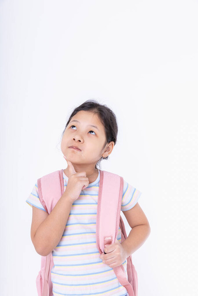 Azjatyckie dzieci dziewczyna cute stoi myśląc. Dzieci z różowymi plecakami chodzą do szkoły na białym tle z przestrzenią do kopiowania, aby przygotować się do nauki. Leaning, Powrót do koncepcji szkoły.  - Zdjęcie, obraz