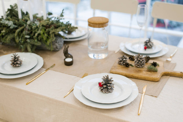 Kerst feestelijke tafel dekken van een feestelijk diner. Dennenappel op een witte plaat - Foto, afbeelding