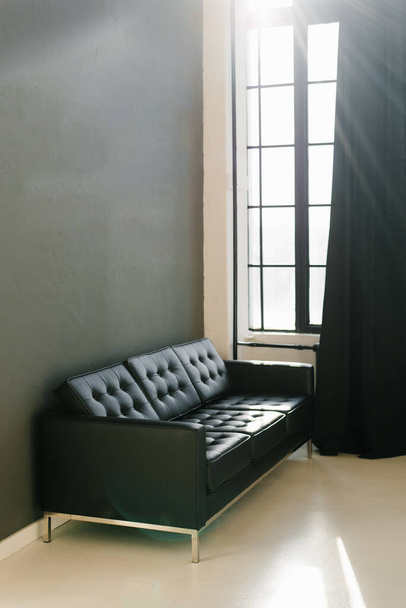 Un canapé noir brutal dans une pièce avec des murs gris foncé et des rideaux noirs sur la fenêtre - Photo, image