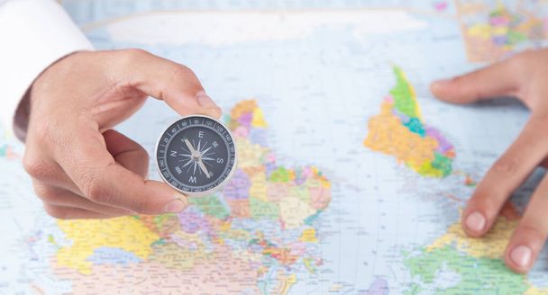 Male hand showing compass on the world map background. - Φωτογραφία, εικόνα