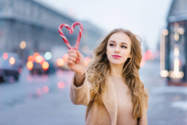 Une douce fille rêveuse, une jeune femme tenant une sucette sous la forme d'un cœur un jour d'hiver. Le concept de Noël ou Saint-Valentin - Photo, image