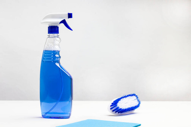 Μπλε μπουκάλια υγρού, κουρέλι και πινέλο στο τραπέζι. Οικιακά χημικά για τον καθαρισμό του διαμερίσματος. Λευκό φόντο. Άνω όψη - Φωτογραφία, εικόνα