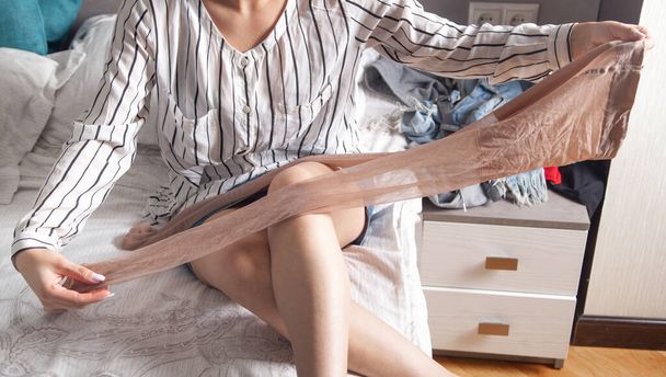 Young woman holding tights in bed. - Φωτογραφία, εικόνα
