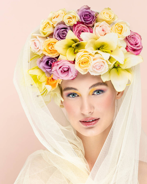 Young beautiful woman with bouquet of flower in head. Art portrait of sexy blonde with colorful flowers. Professional art makeup. Pretty pink background. Happy concept - Fotó, kép