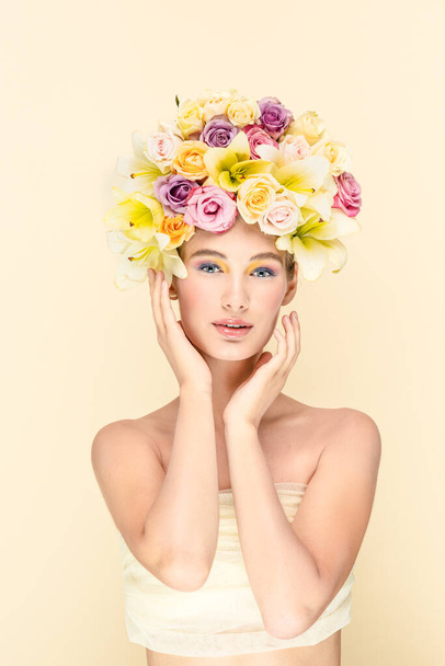 Studio portrait of a young girl with flowers instead of hairstyles, looks into the camera. On a gentle yellowish background  - Foto, Imagem