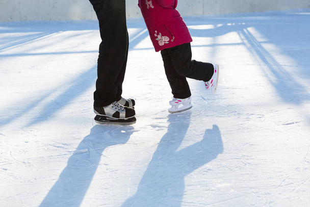Dad teaches his little daughter to ice skate on a skating rink in the courtyard of multi-storey buildings in the city. Frosty winter sunny day, active winter sports and lifestyle - Fotoğraf, Görsel