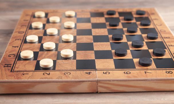 Checkers game on checkerboard in wooden background. - Photo, Image