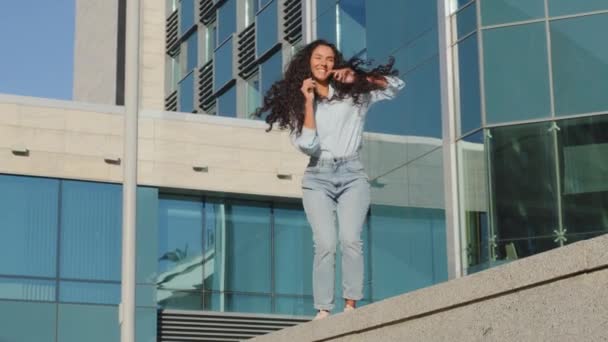 Χαρούμενη χαρούμενη ανέμελη κοπέλα που κινείται ενεργά χορεύτρια γυναίκα με μακριά μαλλιά κυρία φοιτητής νικητής χορό κινείται ρυθμικά στη μουσική χαριτωμένη κινήσεις κοντά στο κτίριο της πόλης απολαμβάνοντας το Σαββατοκύριακο διακοπές καλοκαίρι ημέρα - Πλάνα, βίντεο