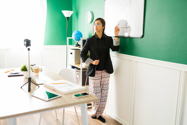 Latijnse jonge vrouw die virtuele les geeft met een pyjamabroek. Vrouwelijke leraar doet een live stream voor haar online studenten - Foto, afbeelding