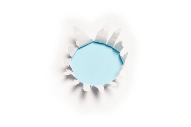 Un agujero en un papel blanco sobre un fondo azul, copiar espacio.  - Foto, Imagen
