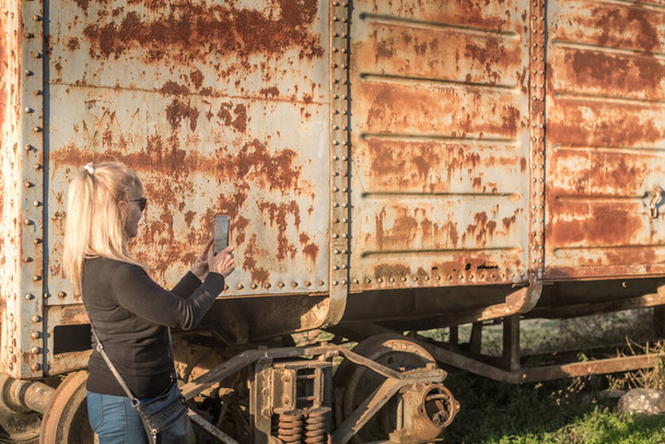 Femme adulte blonde prenant une photo avec son smartphone de voitures abandonnées - Photo, image