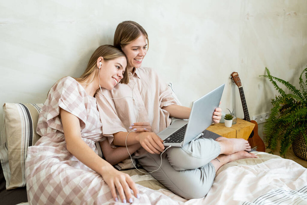 Two smiling restful girls with laptop watching movie - Foto, Imagen