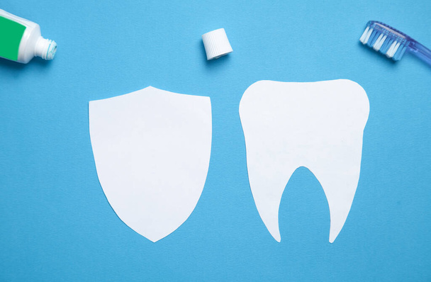 Papírový zub se zubním kartáčkem a zubní pastou na modrém pozadí. - Fotografie, Obrázek