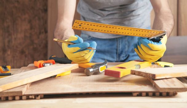 Carpenter holding pencil and measure level. Making marks on wooden planks - Foto, afbeelding