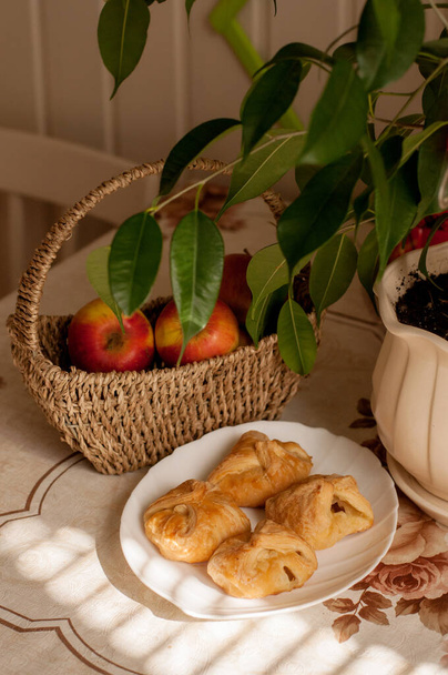 puff pastry pies on a white plate against the background of apples and houseplant - Фото, изображение
