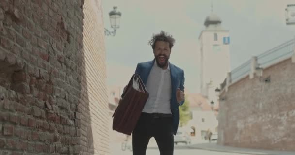 νεαρός επιχειρηματίας που αισθάνεται ενθουσιασμένος, χορεύει στην πόλη με ενέργεια, κρατάει ένα χαρτοφύλακα και χαζολογάει - Πλάνα, βίντεο