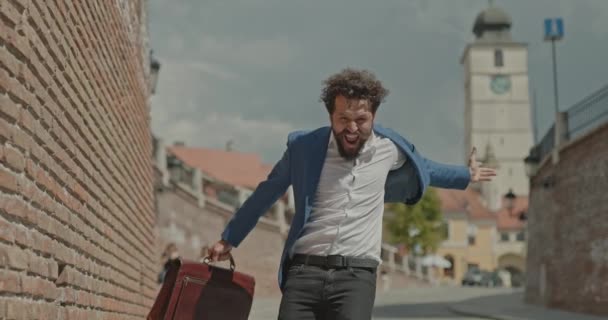young businessman pulling his jacket then starting to dance with excitement, jumping, holding a briefcase and pointing at the camera - Footage, Video