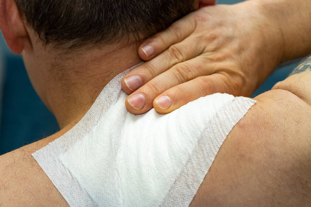 Warming patch glued to the neck, The man is holding on to the sore cervical spine. - 写真・画像