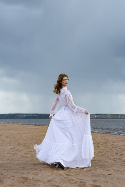 Joyeux jeune fille en robe blanche sur le rivage sablonneux. Ciel tonnerre  - Photo, image