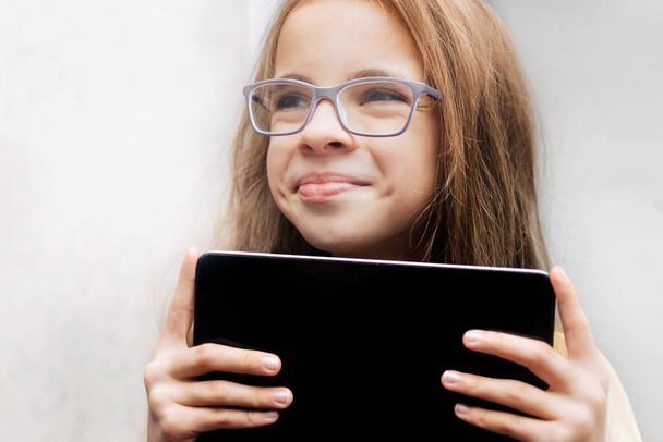 Entrenamiento en línea. Estudia en casa. Retrato de una chica elegante y linda con gafas sosteniendo un plato negro tableta. espacio de copia. - Foto, imagen