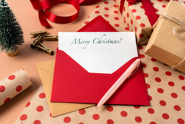Χριστουγεννιάτικη κάρτα με ευχές σε κόκκινο φάκελο στο φόντο του περιτυλίγματος δώρων. Κλείσε. - Φωτογραφία, εικόνα