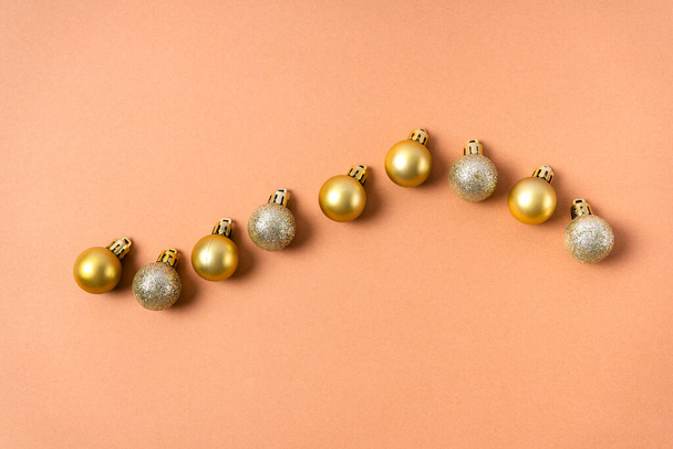 Золотые сверкающие шары на елке выкладываются в ряд на бежевом фоне. Рождественские украшения - Фото, изображение