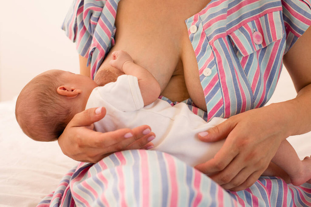 The mom is breastfeeding her newborn baby on the bed - Foto, Bild