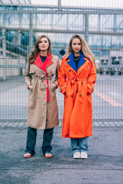 Fashionable happy smiling blonde woman wearing orange coat, blue jeanse and neckchain communicate with her girlfriend on the street. - Fotoğraf, Görsel