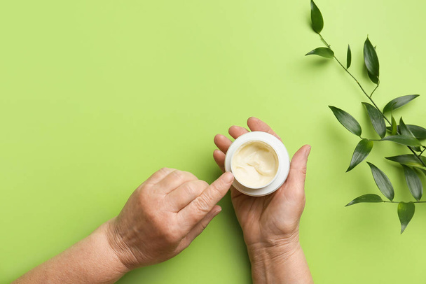 Hands of elderly woman with jar of cosmetic cream on color background - Photo, Image