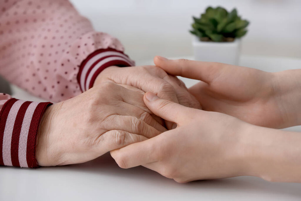 Young woman holding hands of grandmother at table - Photo, Image