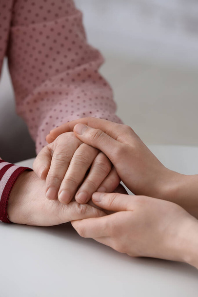 Young woman holding hands of grandmother at table - Photo, Image