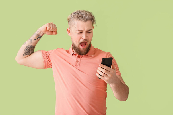 Happy young man with modern mobile phone on color background - Foto, afbeelding