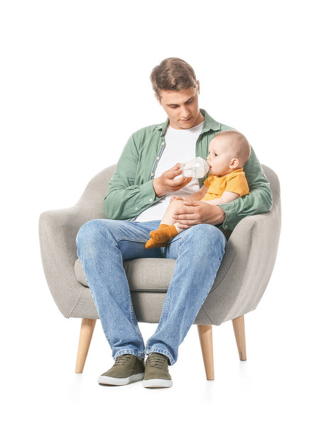 Junger Vater füttert kleines Baby im Sessel auf weißem Hintergrund - Foto, Bild