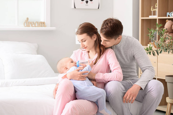 Young parents feeding little baby boy with bottle in bedroom - Фото, зображення