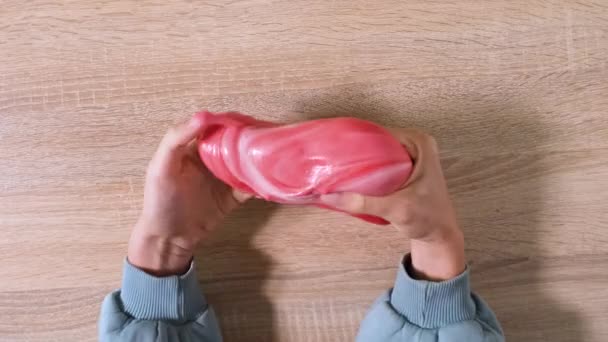 Playing with slime, stretching the gooey substance for fun and stress relief. Close up and top view of female hand holding red and white shining slime and squeezing it. 4K video. - Footage, Video