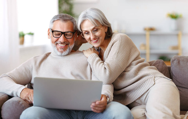 Heureux couple de personnes âgées regardant la comédie ou drôle de vidéo sur ordinateur portable tout en passant du temps libre à la maison - Photo, image