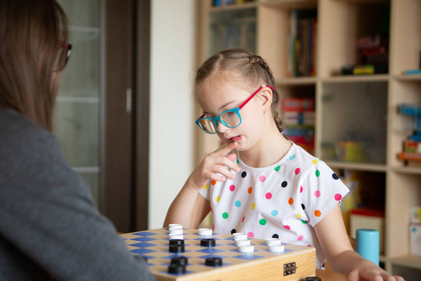 Дівчинка з синдромом Дауна грає в шашки. - Фото, зображення