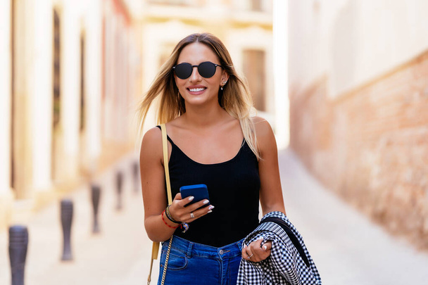 Smiling woman browsing smartphone in city - Valokuva, kuva