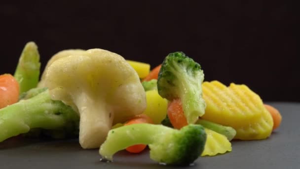 Čerstvě zmrazená zelenina rotující na černém pozadí, zdravé potraviny nebo dietní potraviny pro vegetariány a vegany, mražený květák, brokolici a mrkev pro kojence - Záběry, video