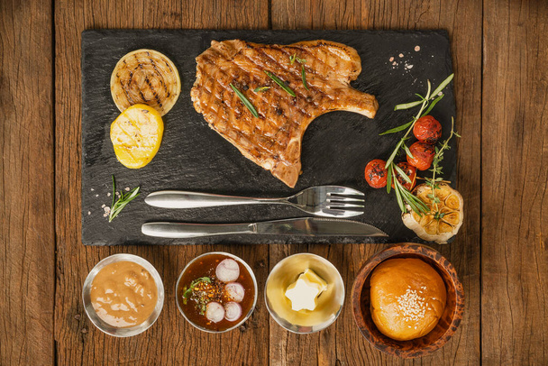 top view of pork chop steak on stone plate with sauce and butter and bread for restaurant manu - Zdjęcie, obraz